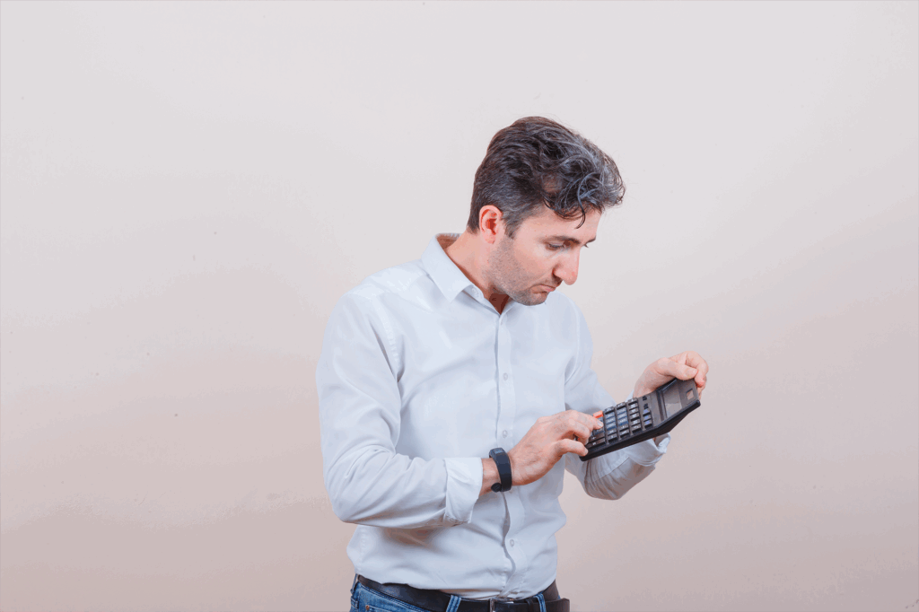 Jovem de camisa branca, jeans usando calculadora e parecendo ocupado