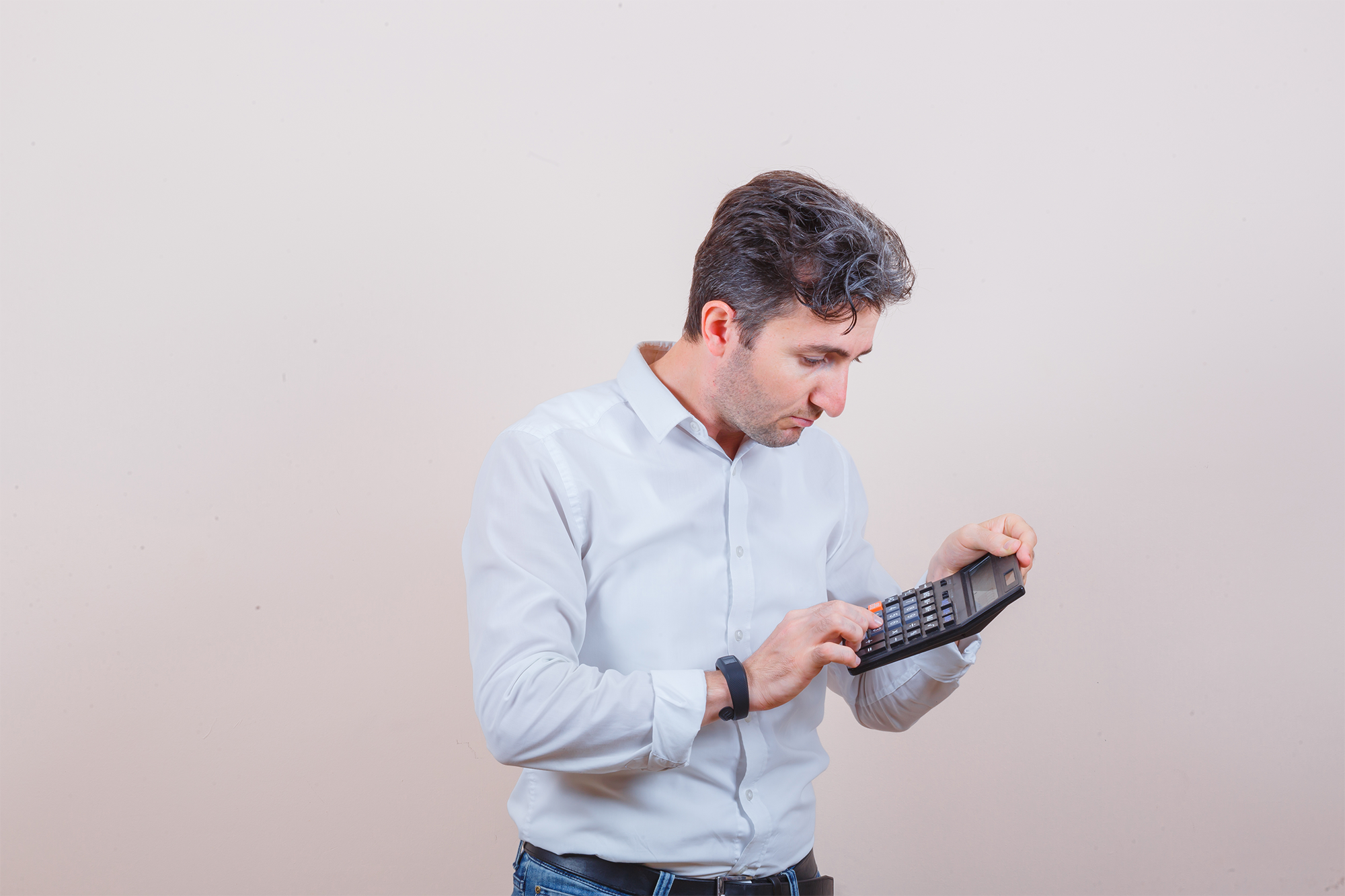 Jovem de camisa branca, jeans usando calculadora e parecendo ocupado