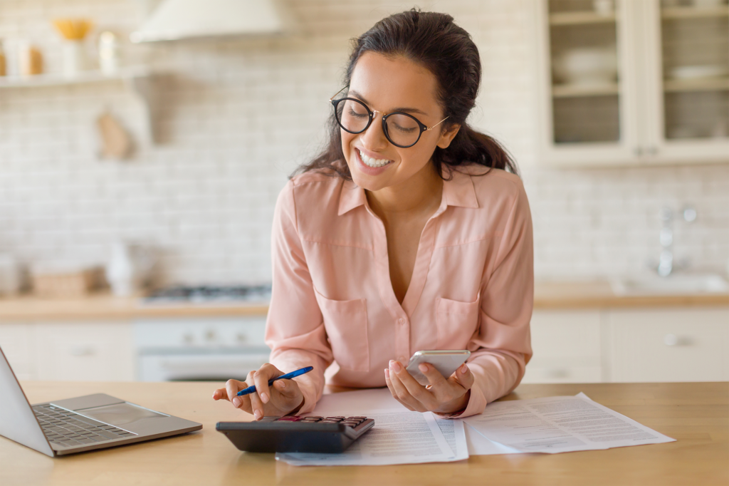 Mulher sorridente na mesa da cozinha com laptop e calculadora