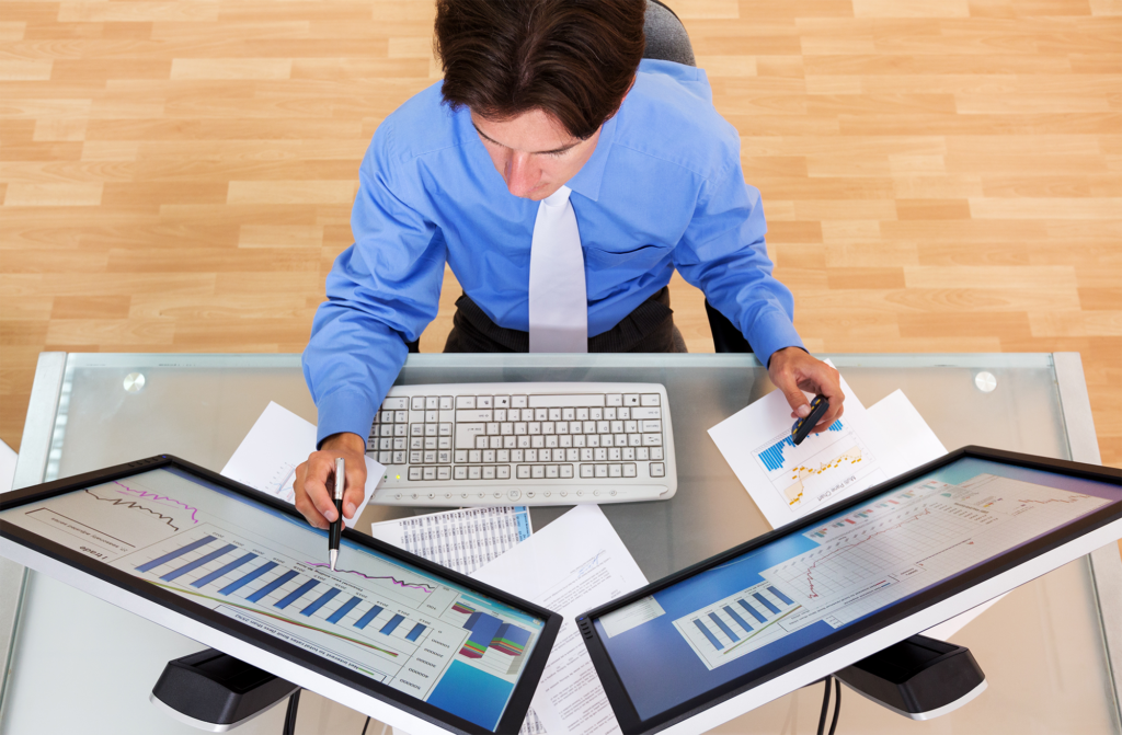 Retrato de um empresário analisando tabelas e gráficos em monitores de computador, vista superior