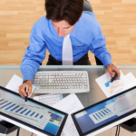 Retrato de um empresário analisando tabelas e gráficos em monitores de computador, vista superior