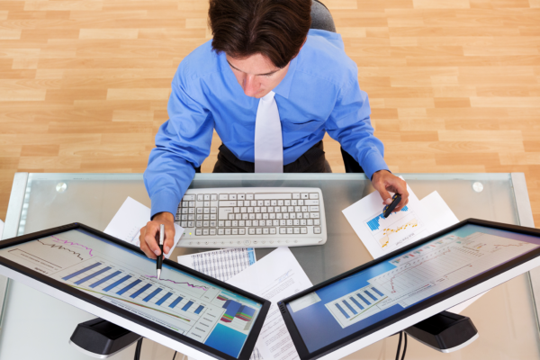 Retrato de um empresário analisando tabelas e gráficos em monitores de computador, vista superior