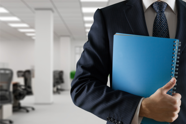 Empresário segurando caderno com capa azul contra seu corpo